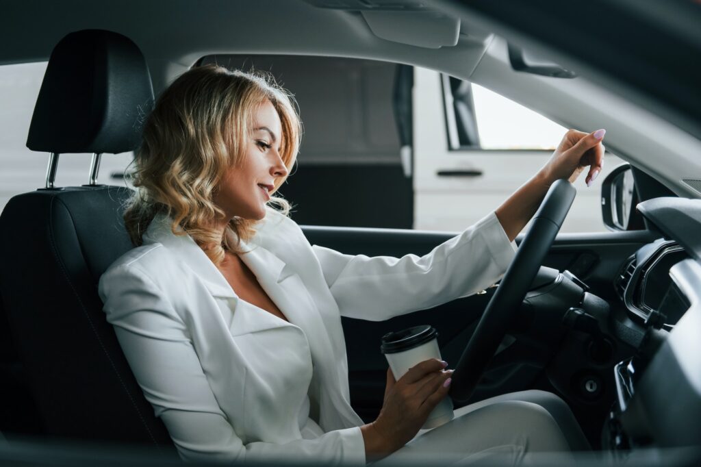 In the car. Woman in formal clothes is indoors in the autosalon