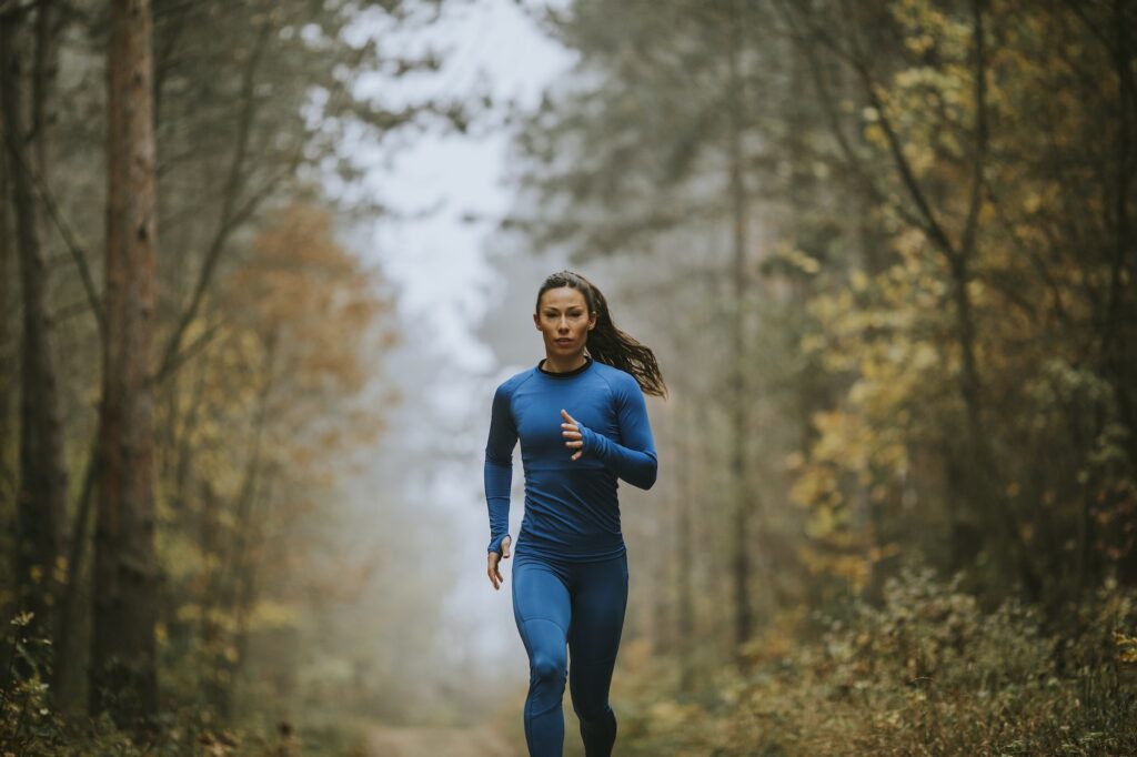 Young woman running toward camera on the forest trail at autumn
